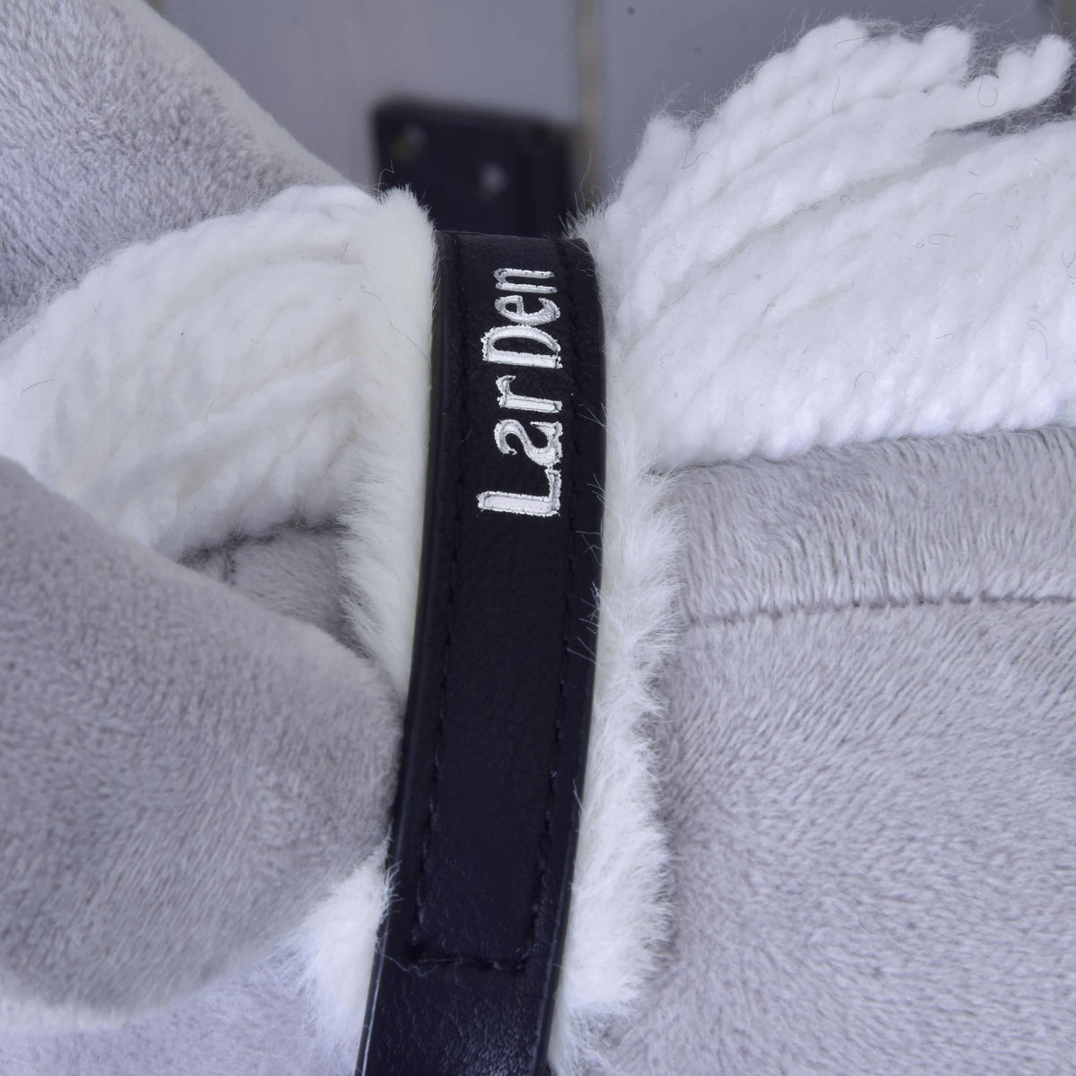 Närbild av det svarta nackstycket med vit broderad LarDen-text och vitt pälsfoder vid manen av garn