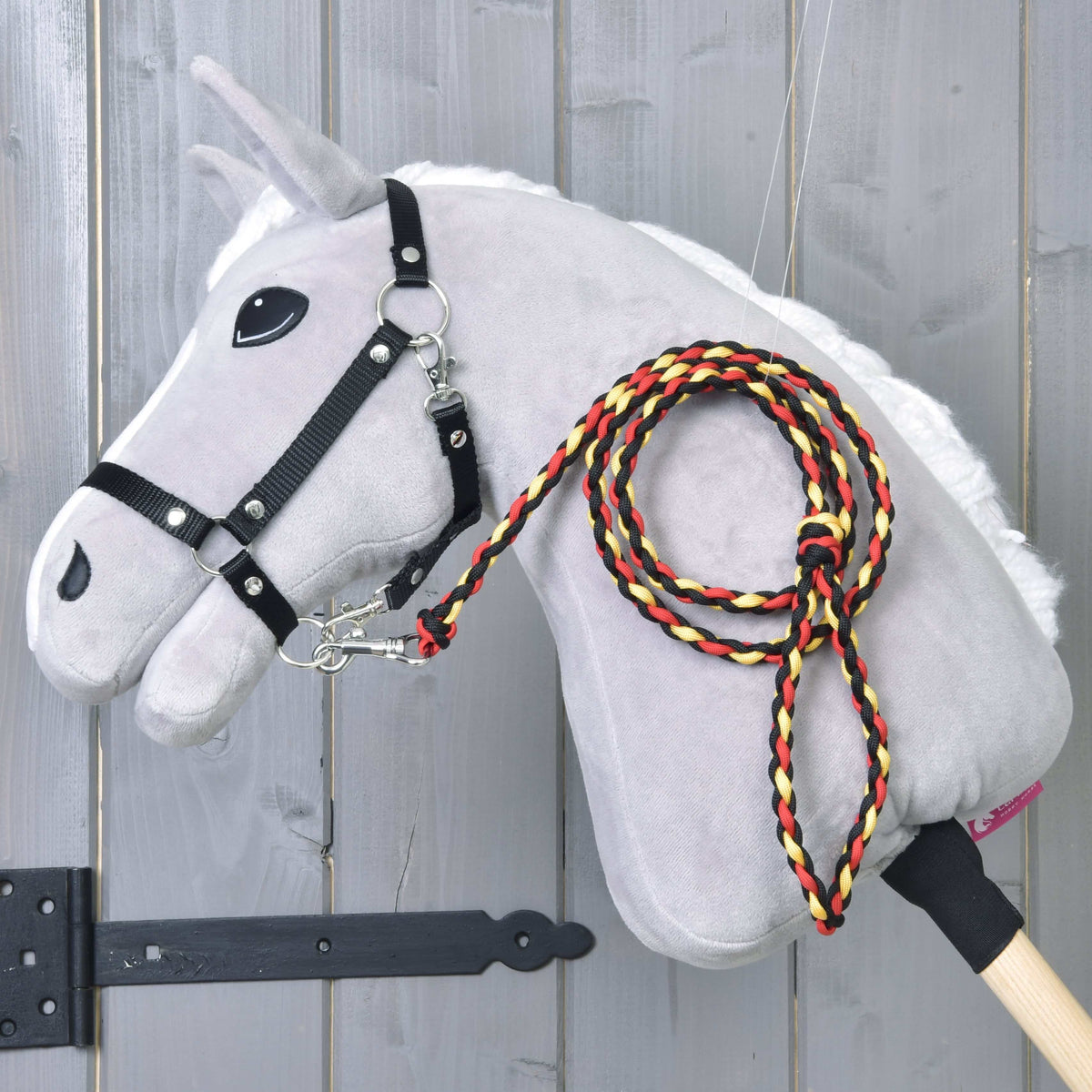 Light grey Hobby Horse in a black halter with the braided black, red and yellow rope stripe Flag lead rope