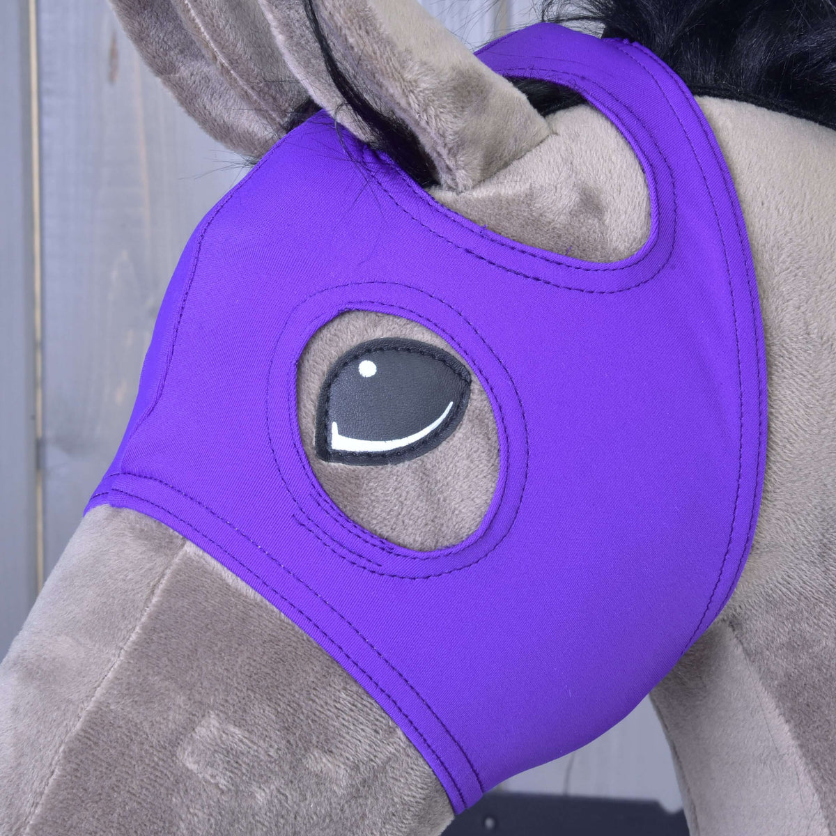 Närbild på den violetta masken på en gråbrun käpphäst, med örat genom öppningen och ett sytt ögonhål
