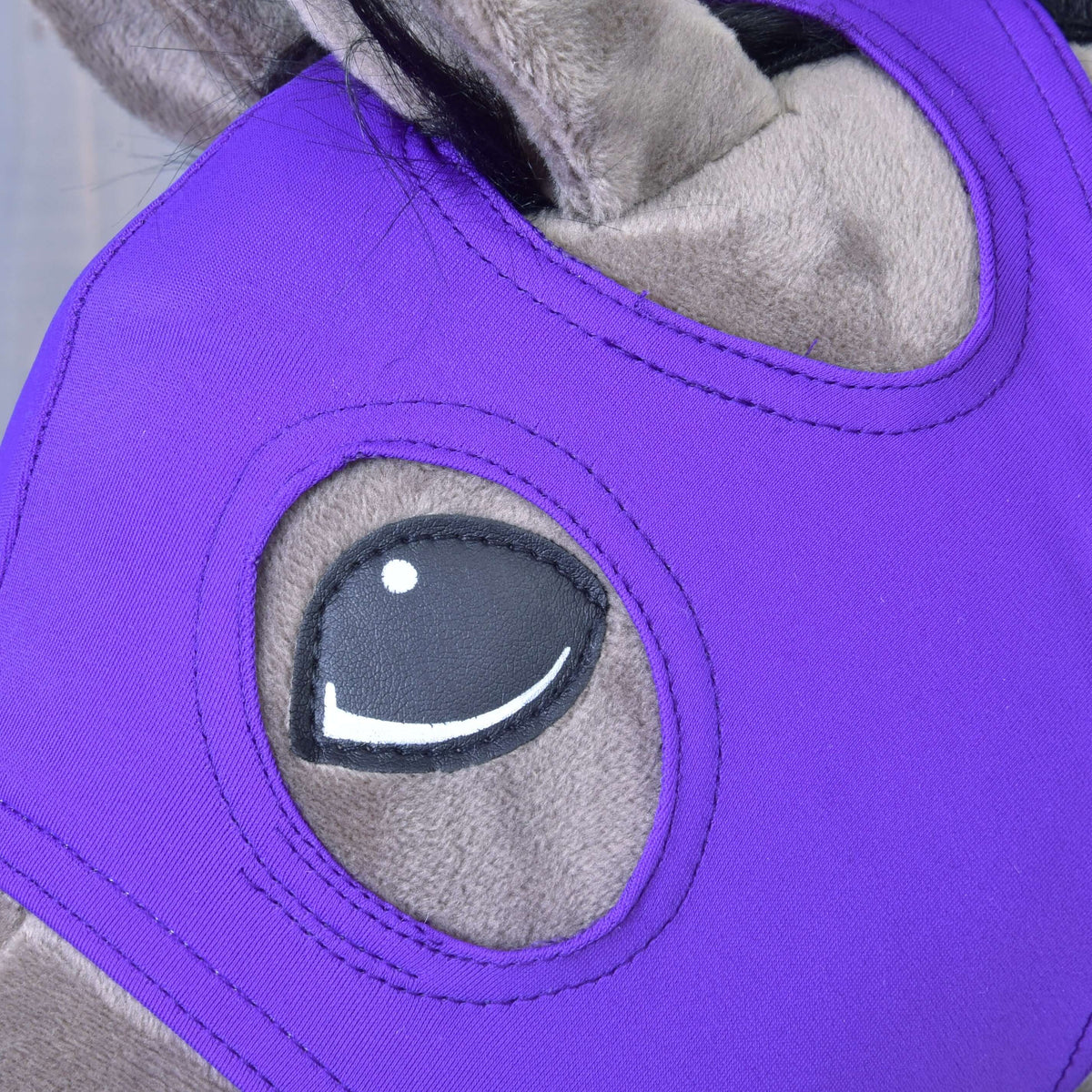 Detalj av den prydligt sydda ögonöppningen i det violetta stretchtyget på masken Indigo, runt ögat på en käpphäst