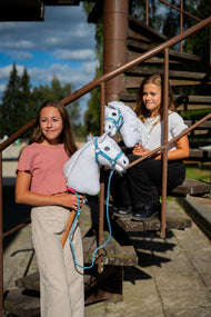 Two girls on a metal staircase with white Hobby Horses in pastel blue halters, one with a braided blue lead rope