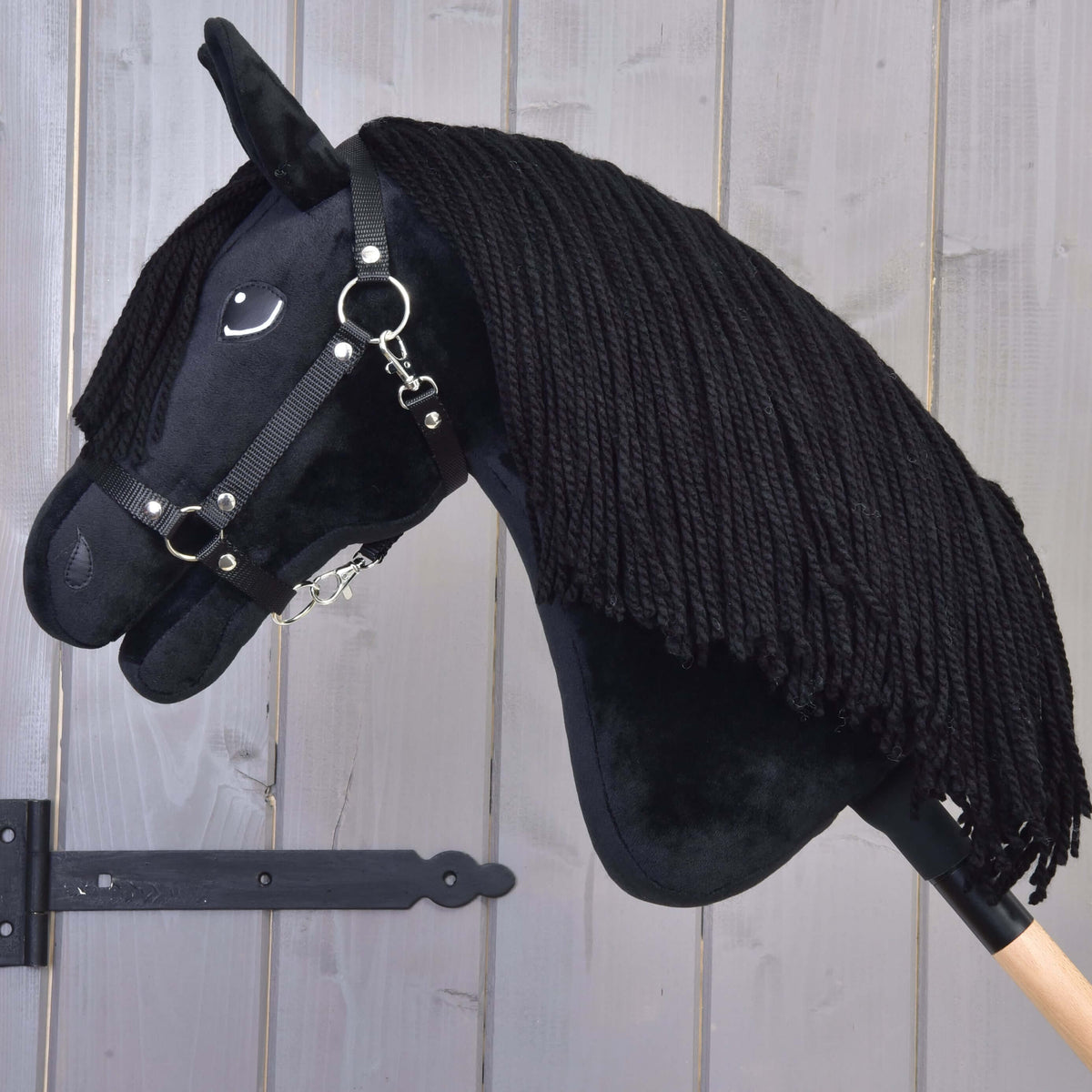 Hobby Horse Mahal med svart grimma med sänkt huvud, tjock svart man av garn faller över den svarta halsen i plysch