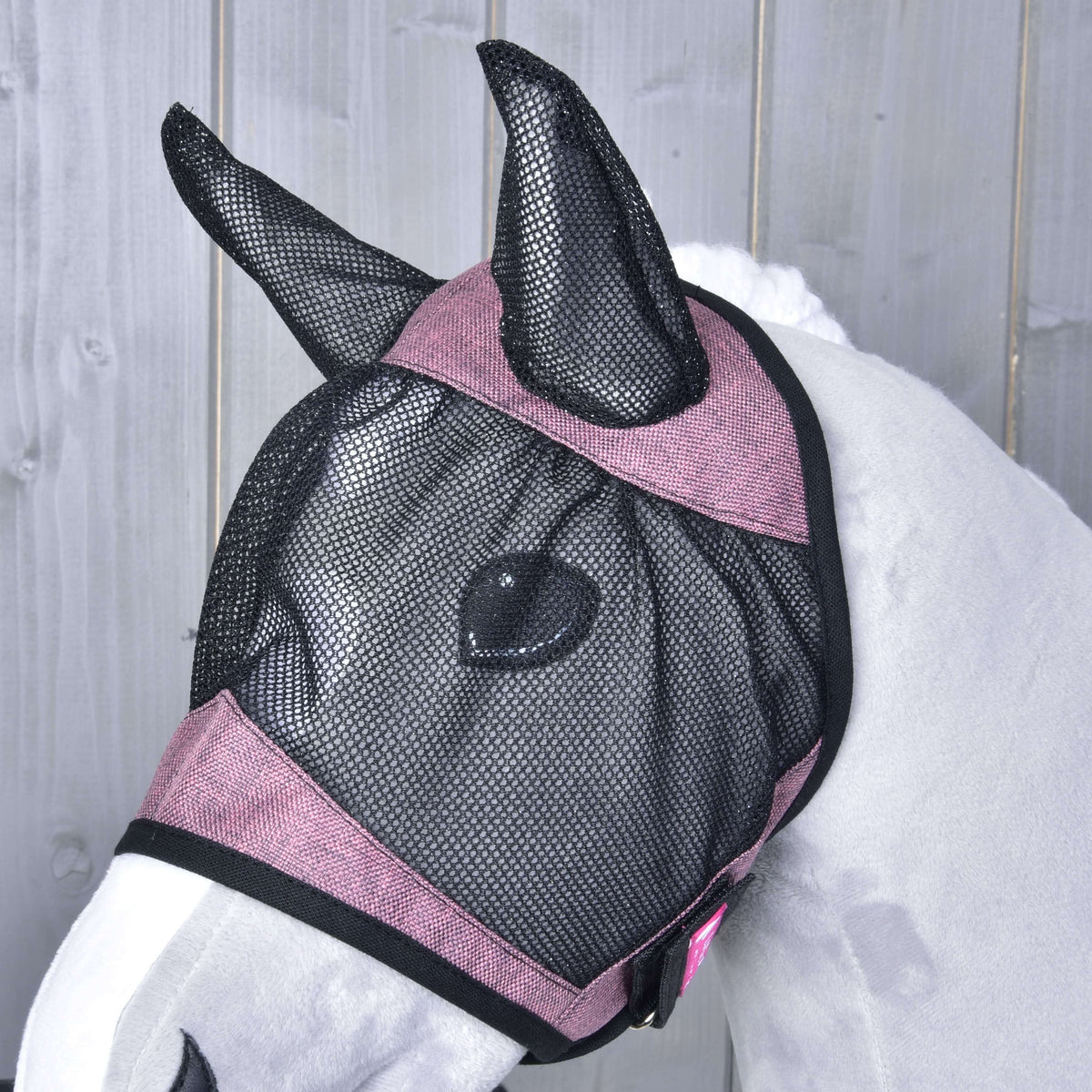 Närbild av flugmasken på en grå käpphäst från sidan, svart nät över ögat och rosa band med svart kant