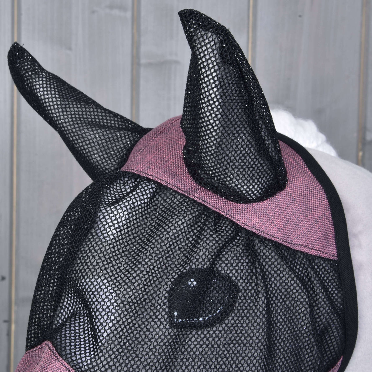 Närbild av öronen av svart nät och det melerade rosa bandet över pannan på flugmasken