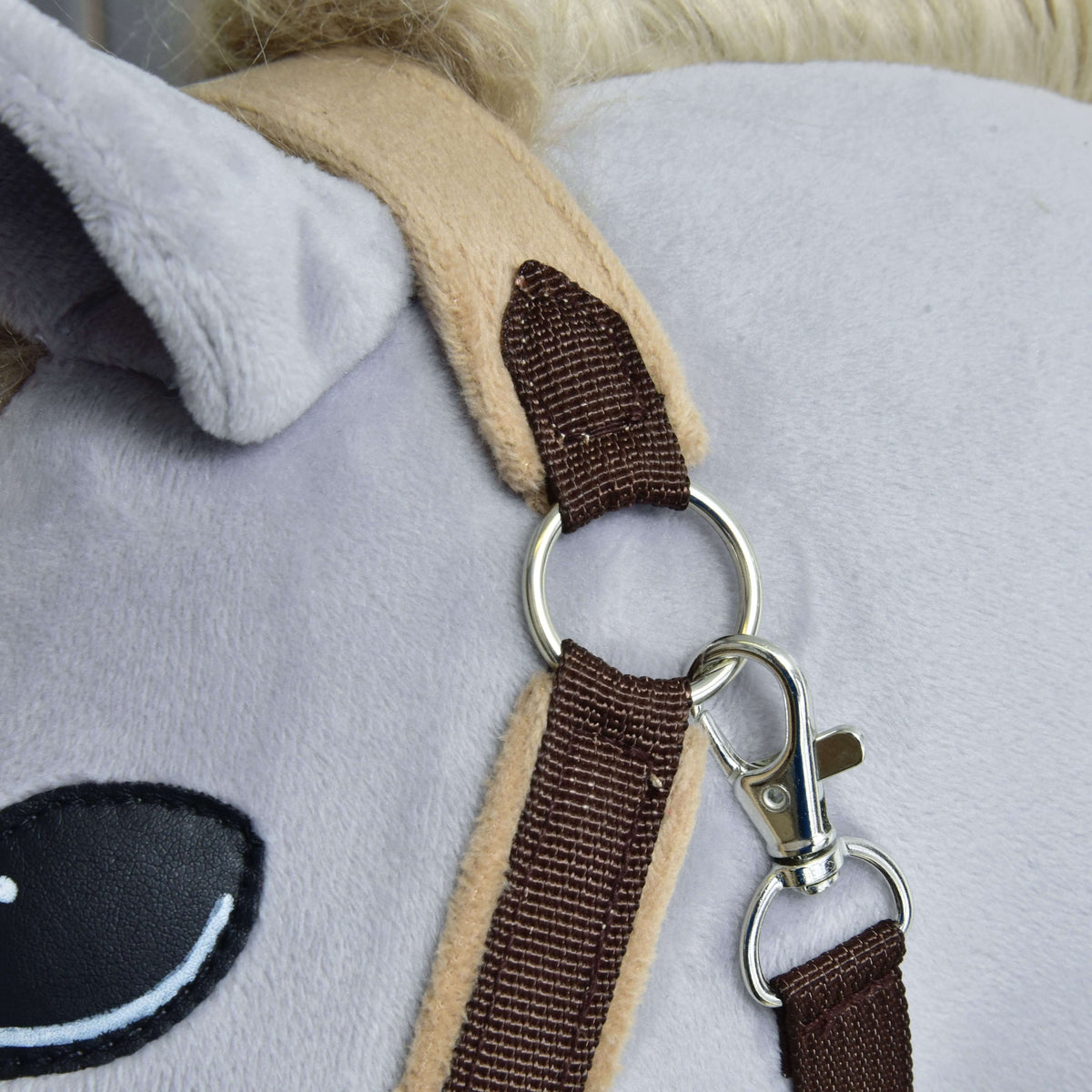 Närbild av den silverfärgade ringen och karbinhaken under örat, där den mörkbruna remmen möter nackstycket i beige fleece
