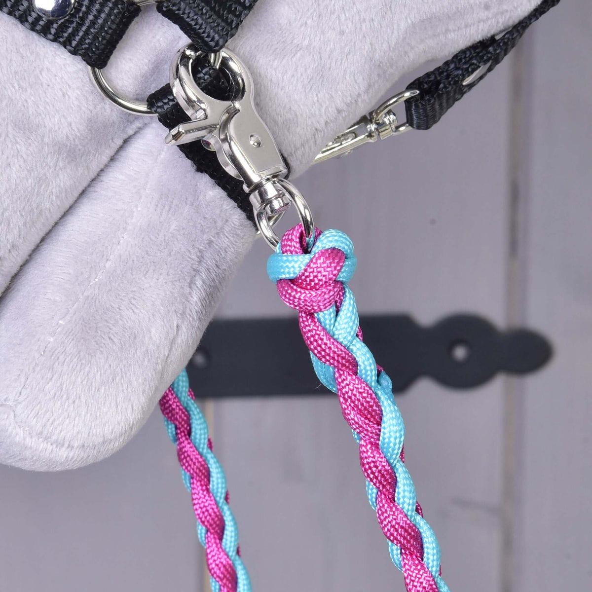 Närbild av en silverfärgad karbinhake på tyglarna Knitted Pinkie Blue fäst i ringen på en svart Hobby Horse grimma