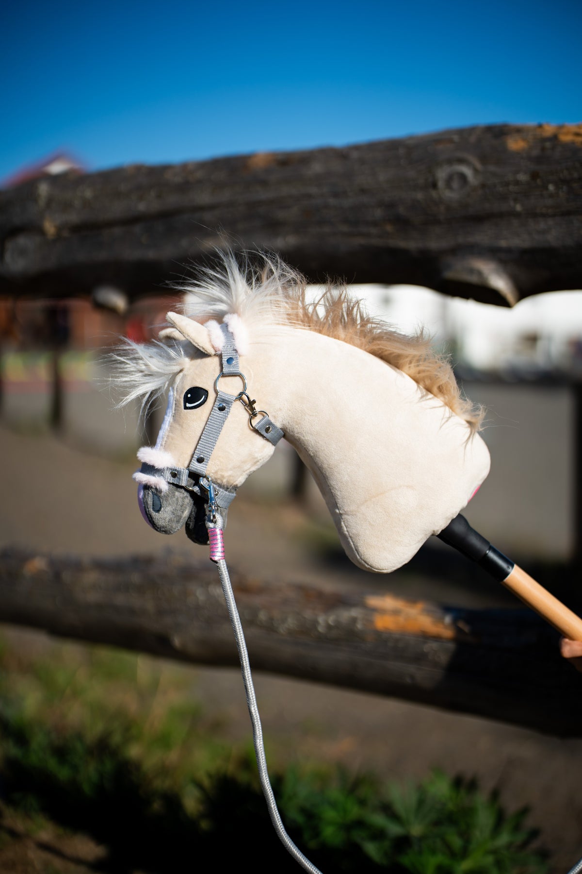 Hobby Horse Pixie in front of a log fence in a grey halter with fur and a grey lead rope with a pink wrap