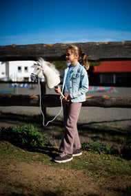 Young girl in a denim jacket at a log fence holding Hobby Horse Pixie in a grey fur halter with a lead rope