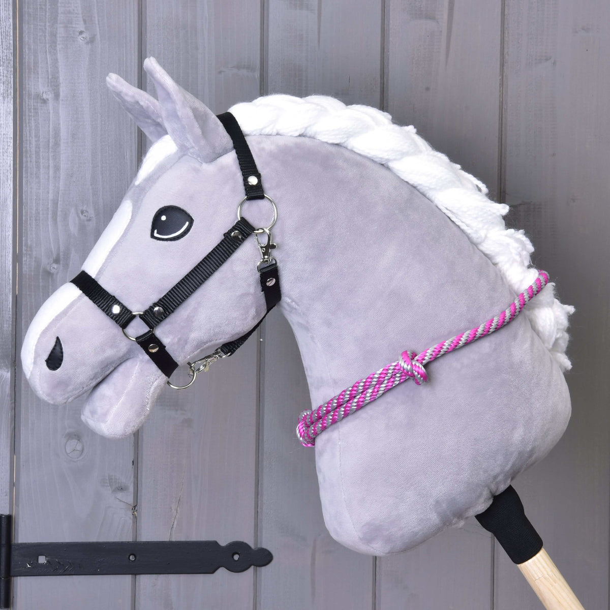 Grå käpphäst i svart grimma med halsringen av rep med rosa och grå ränder runt halsen