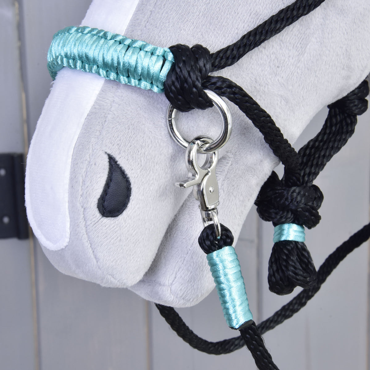 Close-up of the turquoise wrapped noseband, black knots and silver snap clip of the rope halter and reins