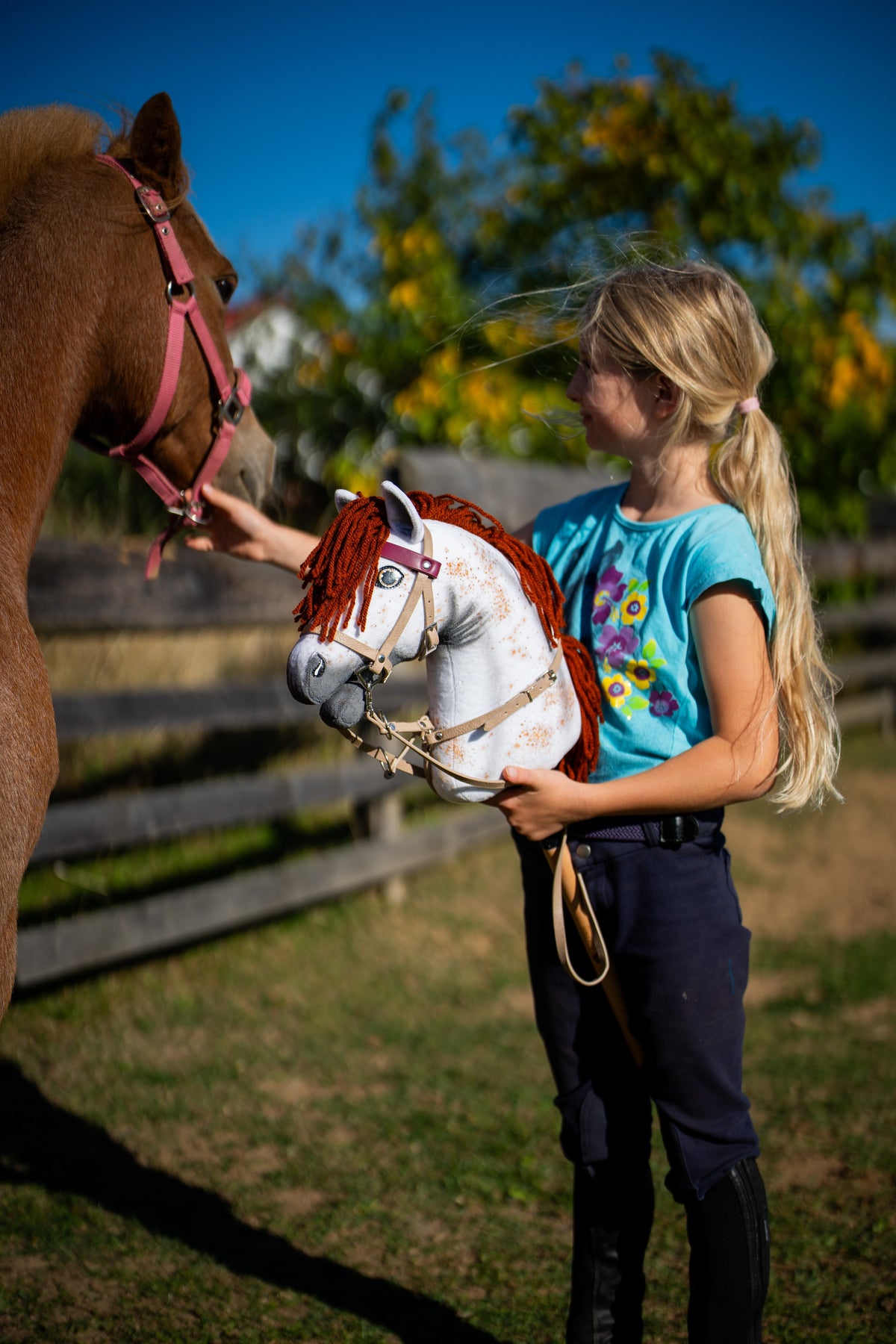 Girl in a turquoise T-shirt with a speckled Hobby Horse in a beige bridle with bordeaux browband next to a chestnut horse