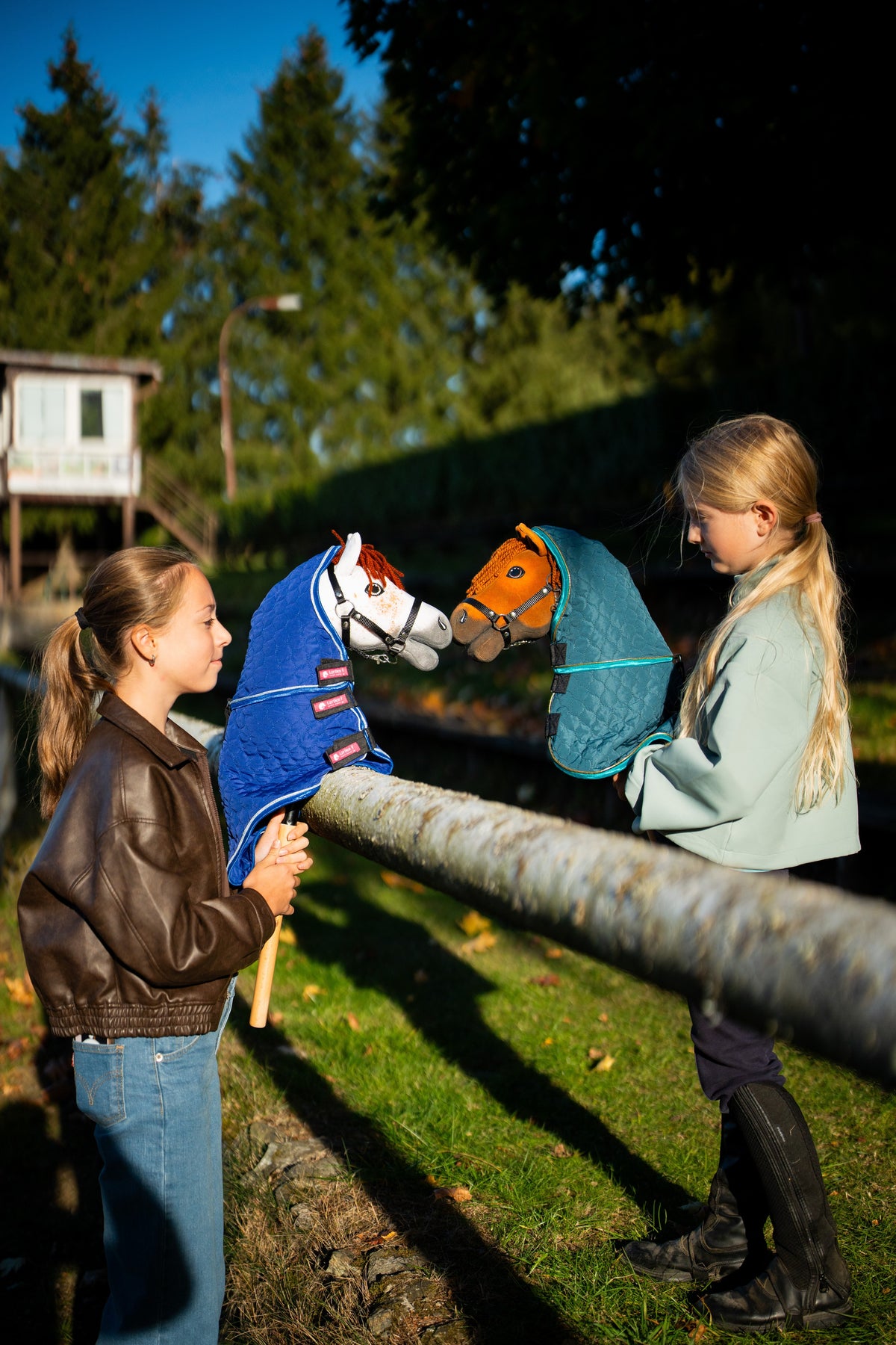 Two girls at a wooden rail with Hobby Horses in quilted blankets with neck covers, Pippa in teal on the right