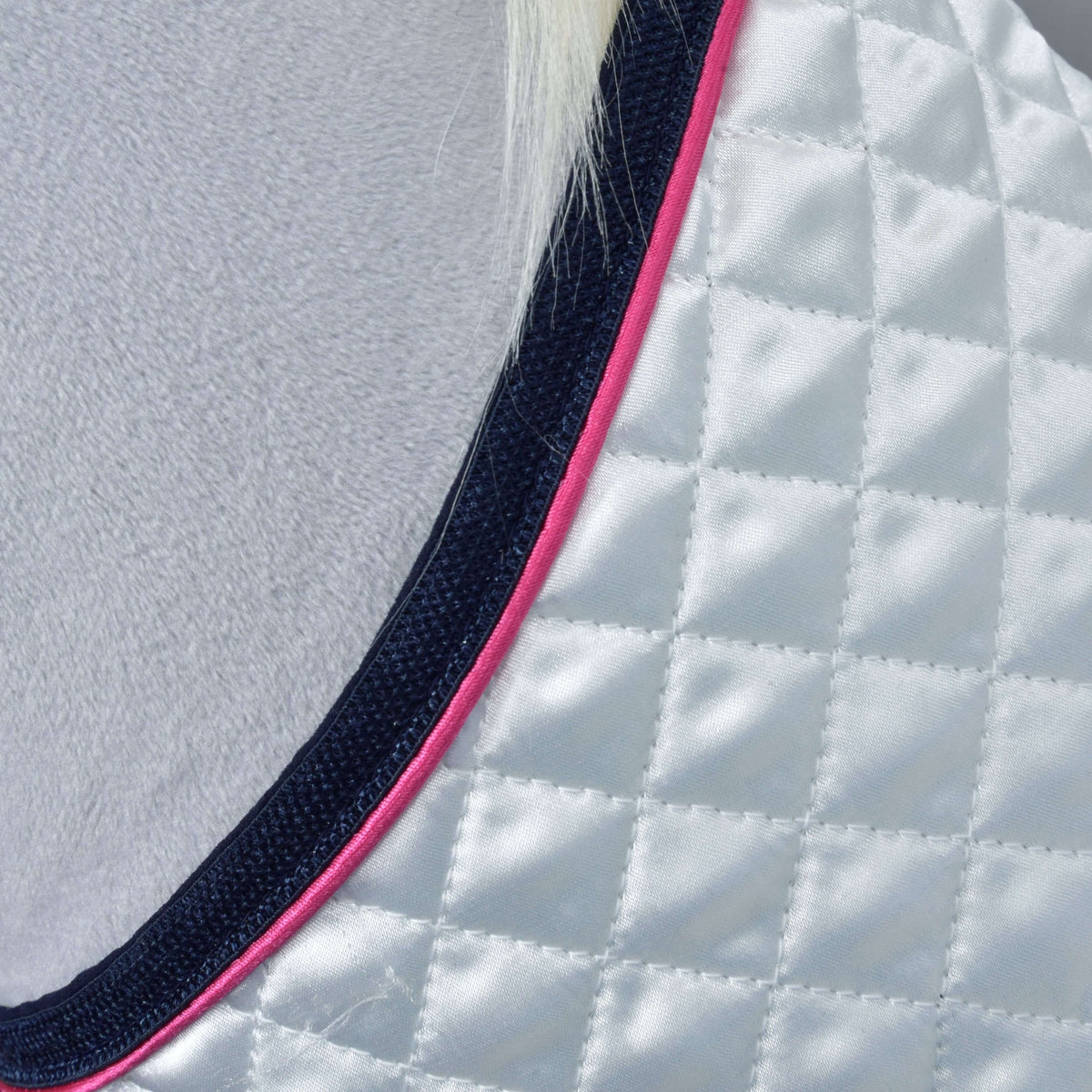 Närbild av den rutquiltade vita satinen med rosa passpoal och marinblått kantband längs täckets halsringning