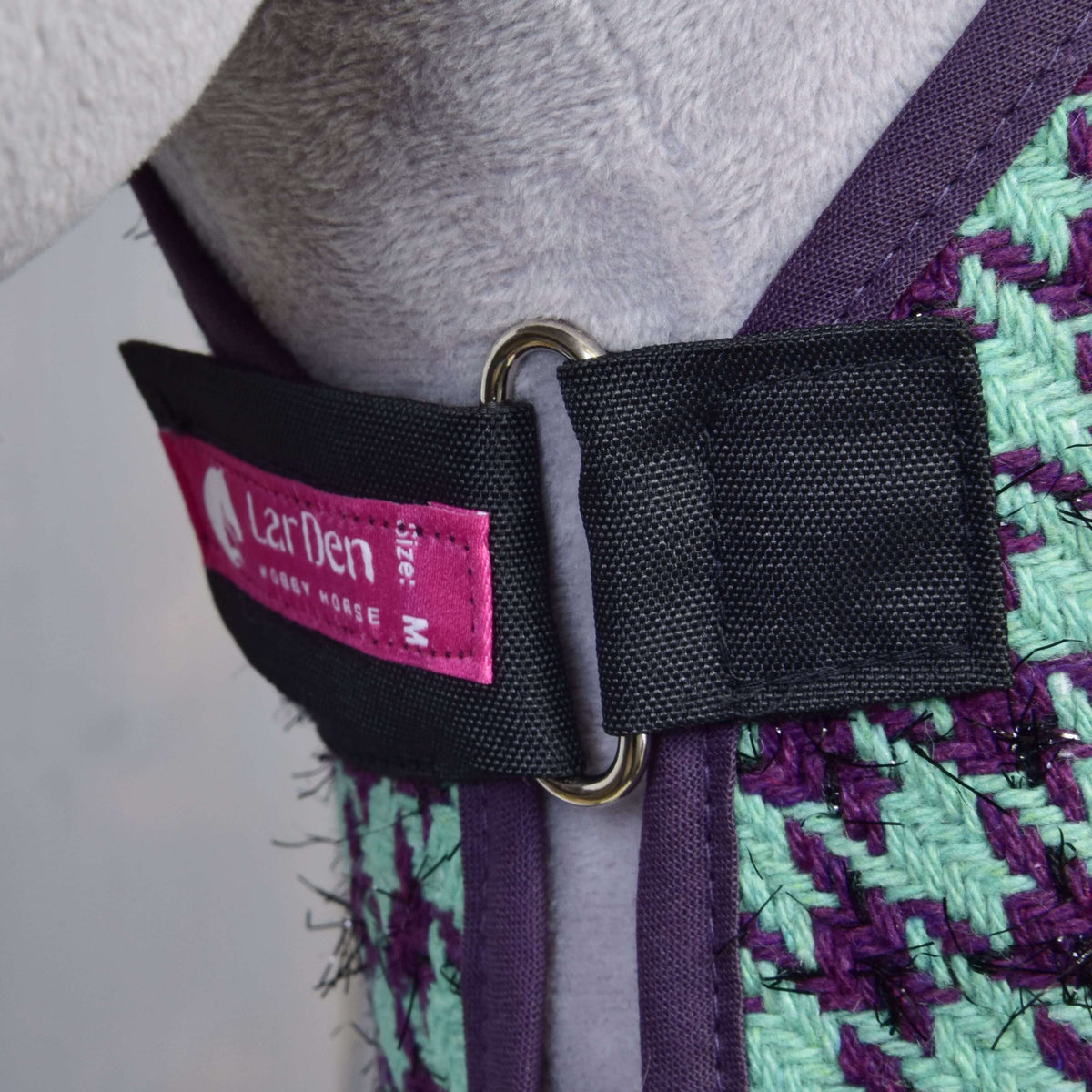 Chest closure of the Set Harmony Green blanket: black strap, metal ring, pink LarDen label and purple binding