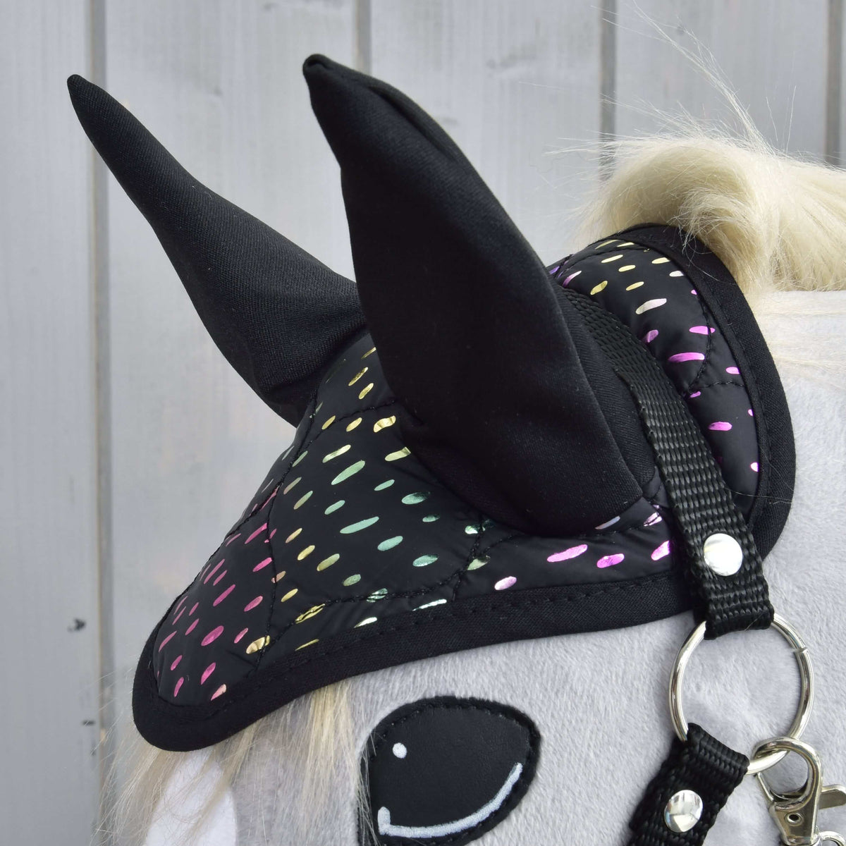 Närbild av flughuvan i set Dreamy med höga svarta öron och skimrande regnbågsprickar, ovanför en svart grimma