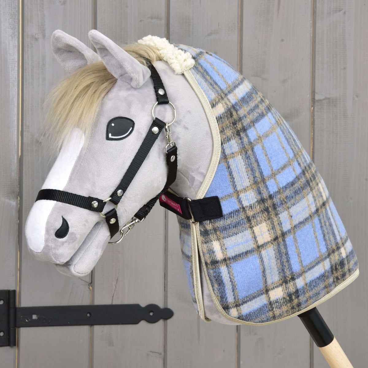 Grey plush Hobby Horse in a black halter wearing the light blue check stable blanket with its black chest strap closed