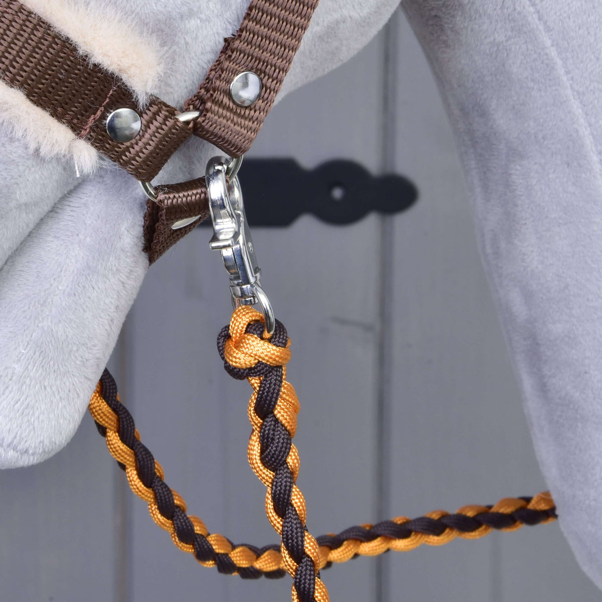 Braided orange and brown ropes hanging from the snap hook under the chin of a grey Hobby Horse in a brown halter