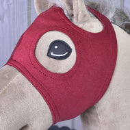 Närbild på den vinröda masken utan öron på en beige käpphäst, med den sydda runda ögonöppningen och örhålet