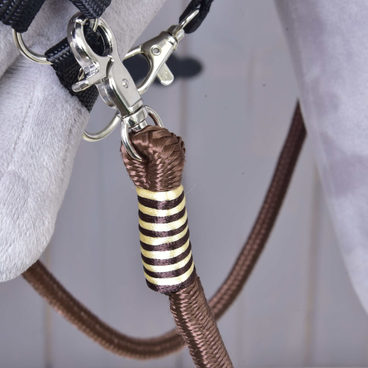 Närbild av den krämfärgade och brunrandiga lindningen på Hobby Horse tyglar Vivaldi under karbinhaken i grimmans ring