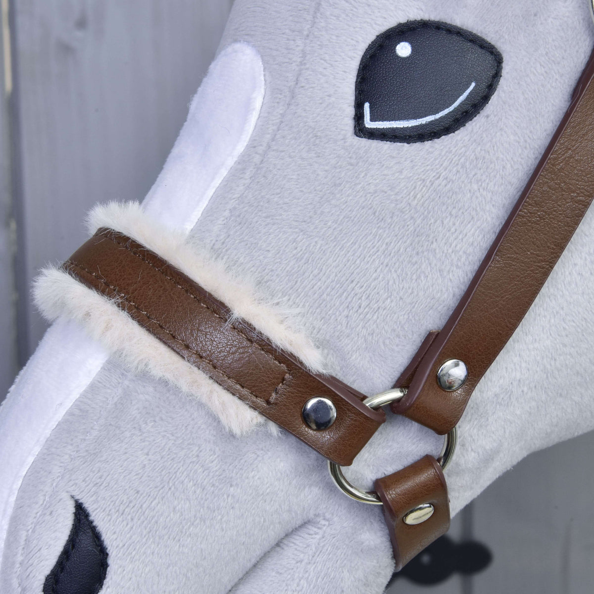 Close-up of the brown leatherette noseband with soft cream fur trim, silver rivets and ring on a grey Hobby Horse