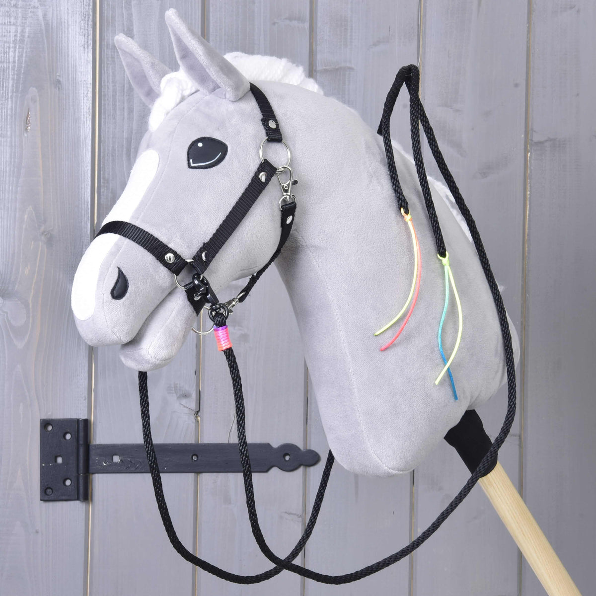 Grey Hobby Horse in a black halter wearing the black western reins, with neon cord tassels hanging on its neck