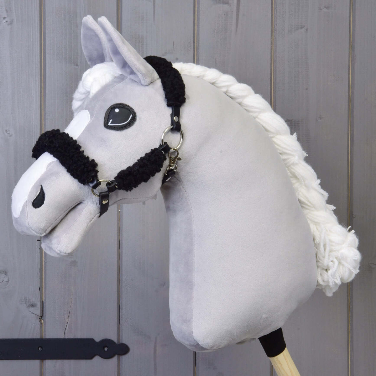Grey plush Hobby Horse with a braided white mane in the black halter with complete black fur, grey wooden wall