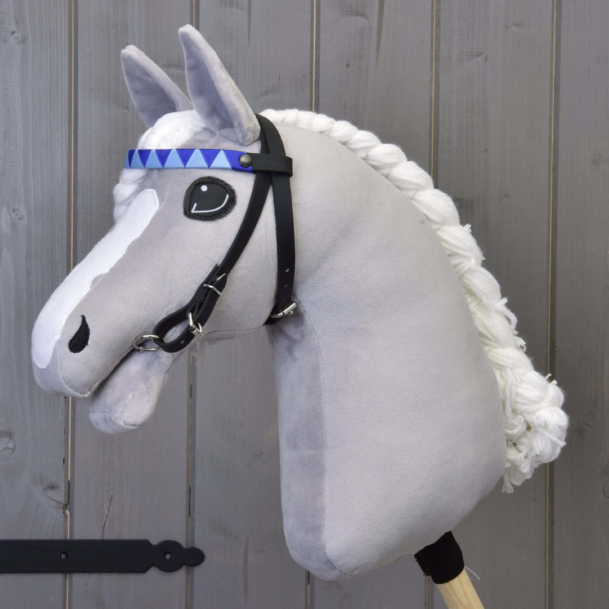 Grey plush Hobby Horse with a braided white mane wearing the black bridle with blue triangle browband