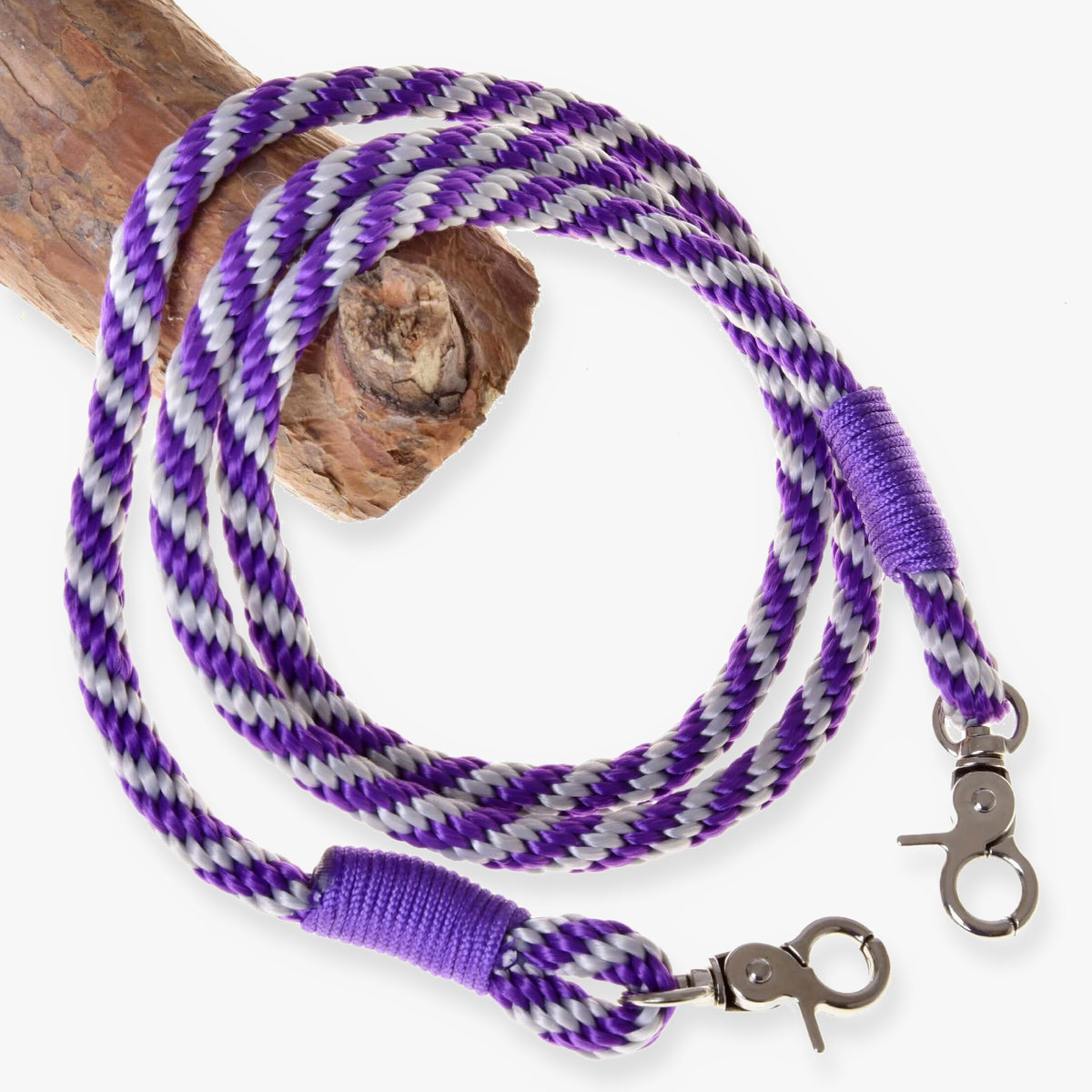 Tyglar med lila ränder för Hobby Horse från LarDen, flätade tyglar av lila och silverfärgat rep med lindade ändar och karbinhakar på en gren