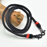 Hobby Horse Reins Spark by LarDen in black braided rope with red wraps and black snap hooks, on a branch
